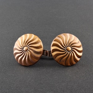 May include: A pair of copper cufflinks with a swirling sunburst design.