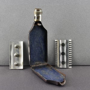 May include: A vintage silver safety razor with a blue velvet case and three blades. The razor has a silver comb and a silver handle.