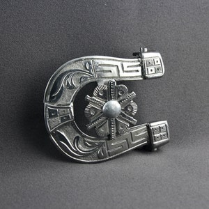 May include: A silver horseshoe-shaped belt buckle with intricate floral designs and a central starburst. The buckle has a polished finish and a detailed design.