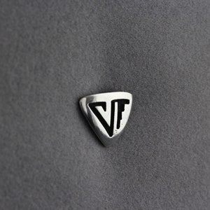 May include: A silver triangular patch with the letters "VF" in black inside.