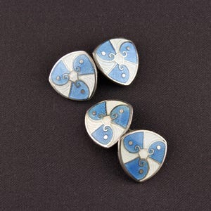 May include: A set of four silver cufflinks with blue and white enamel designs. Each cufflink features a stylized, geometric pattern.