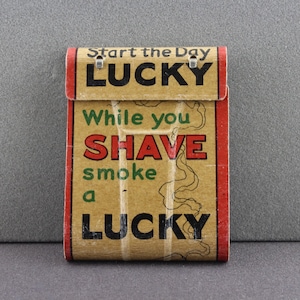 May include: Vintage Lucky Strike cigarette pack advertising with the text "Start the Day Lucky. While you Shave smoke a Lucky."