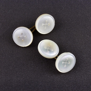 May include: Four mother-of-pearl cufflinks with a cross design on a dark background. The cufflinks have a button-like shape and are connected by a gold-colored bar.