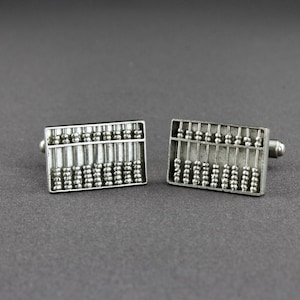 May include: A pair of silver abacus cufflinks. The cufflinks are rectangular and feature a detailed abacus design with beads.