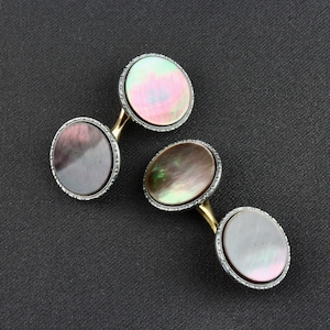 May include: A pair of cufflinks with a black and iridescent mother-of-pearl design. The cufflinks are round and have a silver-toned metal frame.