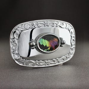 May include: A silver belt buckle with an ornate design and a colorful iridescent butterfly inlay.