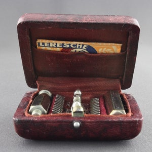 May include: A brown leather case with a small pocket on the inside. The case is open and contains a set of tools, including a small screwdriver, a set of tweezers, and a small metal object. The case is labeled "LERESCHE" on the inside.