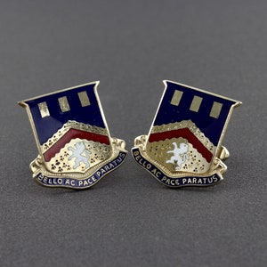May include: A pair of gold cufflinks featuring a blue and red enamel shield design. The shield displays three gold bars, a white lion, and the inscription "BELLO AC PACE PARATUS".