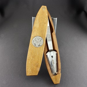 May include: A wooden case with a silver emblem and a metal nail clipper inside. The case is open and the clipper is visible.