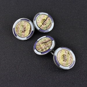 May include: Four vintage cufflinks with a gold, white, and purple design. The cufflinks have a textured gold center with a decorative pattern, surrounded by a white and purple border. The background is a dark gray.