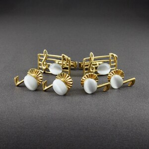May include: A pair of gold cufflinks featuring a musical note design with white opalescent stones. The cufflinks are set against a gray background.