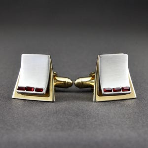 Könnte beinhalten: Ein Paar silberne Manschettenknöpfe mit goldener Einfassung und drei roten Edelsteinen.