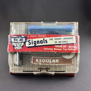 May include: A plastic case with a red, white, and blue label that reads "Signals: The Secret Language of Baseball" and features a baseball player wearing a catcher's mask. The label also says "A Gillette Exclusive" and "Finger-Tip Movies Featuring Manager Paul Richards". The case has a brown label that reads "Regular".