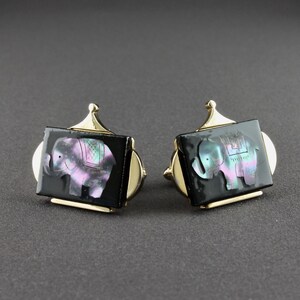 May include: A pair of gold cufflinks with black rectangular bases and iridescent mother-of-pearl elephant designs.