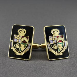 May include: A pair of gold cufflinks with black enamel and a colourful crest design. The crest features a crown, shield, and the text "Omnia Vincit Virtus".