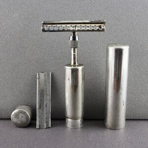 May include: A vintage silver safety razor with a chrome finish and a removable blade. The razor is accompanied by a silver case and a separate blade holder.