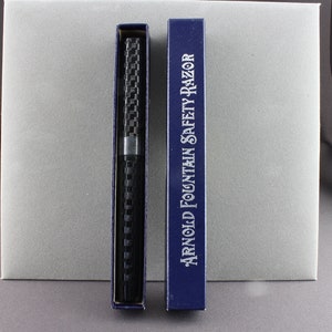 May include: A black and silver safety razor in a blue box with the text "Arnold Fountain Safety Razor".