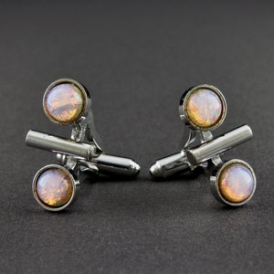 May include: A pair of silver cufflinks with iridescent orange and pink stones. The cufflinks have a simple, geometric design.