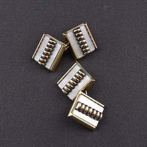 Peut inclure: Quatre boutons de manchette en or avec un incrustation de nacre blanche. Chaque bouton de manchette présente une rangée de perles dorées.