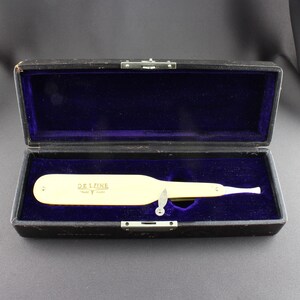 May include: A vintage De Luxe brand straight razor in a black leather case with a blue velvet interior. The razor is made of ivory and has a gold-colored inscription.