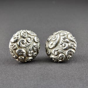 May include: A pair of silver earrings with a detailed, swirling, floral design.