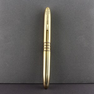 Op de afbeelding: Een gouden metalen pen met een afgeronde punt en drie gouden banden rond de cilinder.