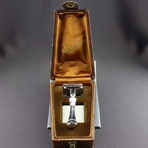 May include: A silver safety razor in a brown leather case with the inscription "Dorwin" on the inside of the lid.