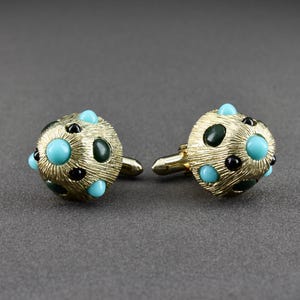 May include: A pair of gold cufflinks with turquoise and black stones. The cufflinks are round and have a textured surface.