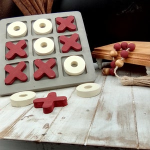 May include: A wooden tic-tac-toe game with red X's and white O's. The game is set on a whitewashed wooden surface.