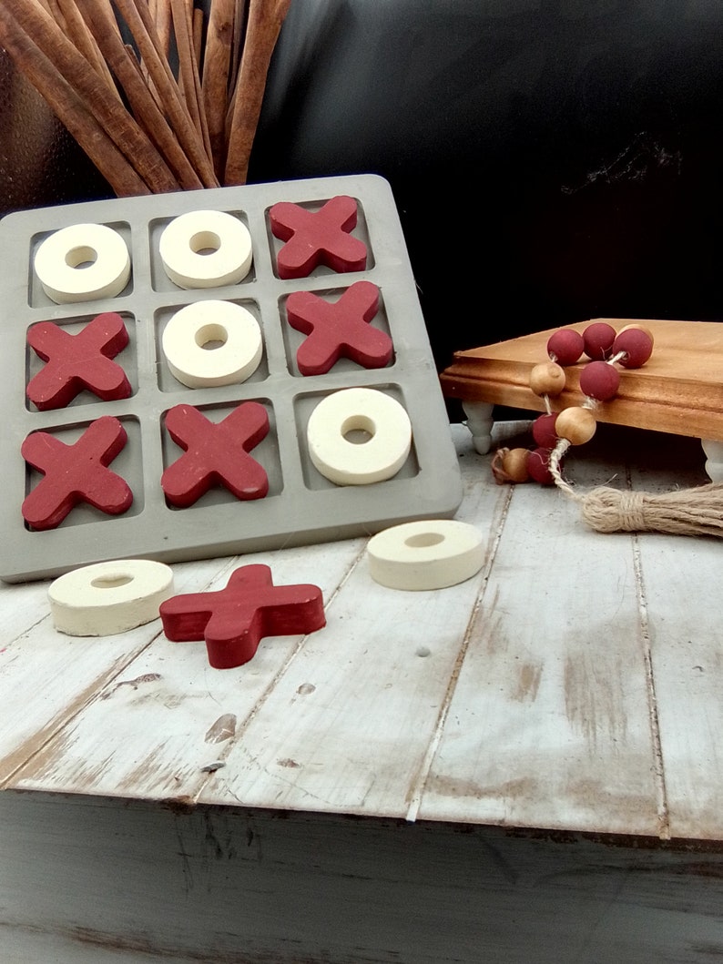 May include: A wooden tic-tac-toe game with red X's and white O's. The game is set on a whitewashed wooden surface.