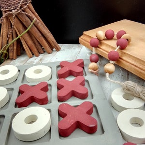 May include: A wooden tic-tac-toe game with red X's and white O's. The game is set on a white wooden surface.