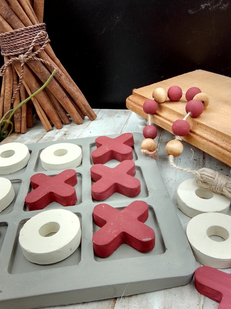 May include: A wooden tic-tac-toe game with red X's and white O's. The game is set on a white wooden surface.