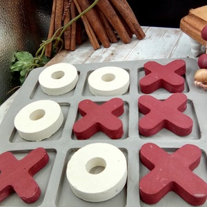 May include: A gray wooden tic-tac-toe game board with white circles and red X's. The board is made of wood and has a rustic look.