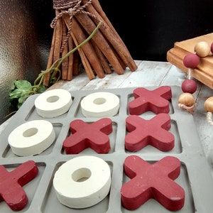 May include: A gray wooden tic-tac-toe game with red X's and white O's. The game is set up on a gray surface.