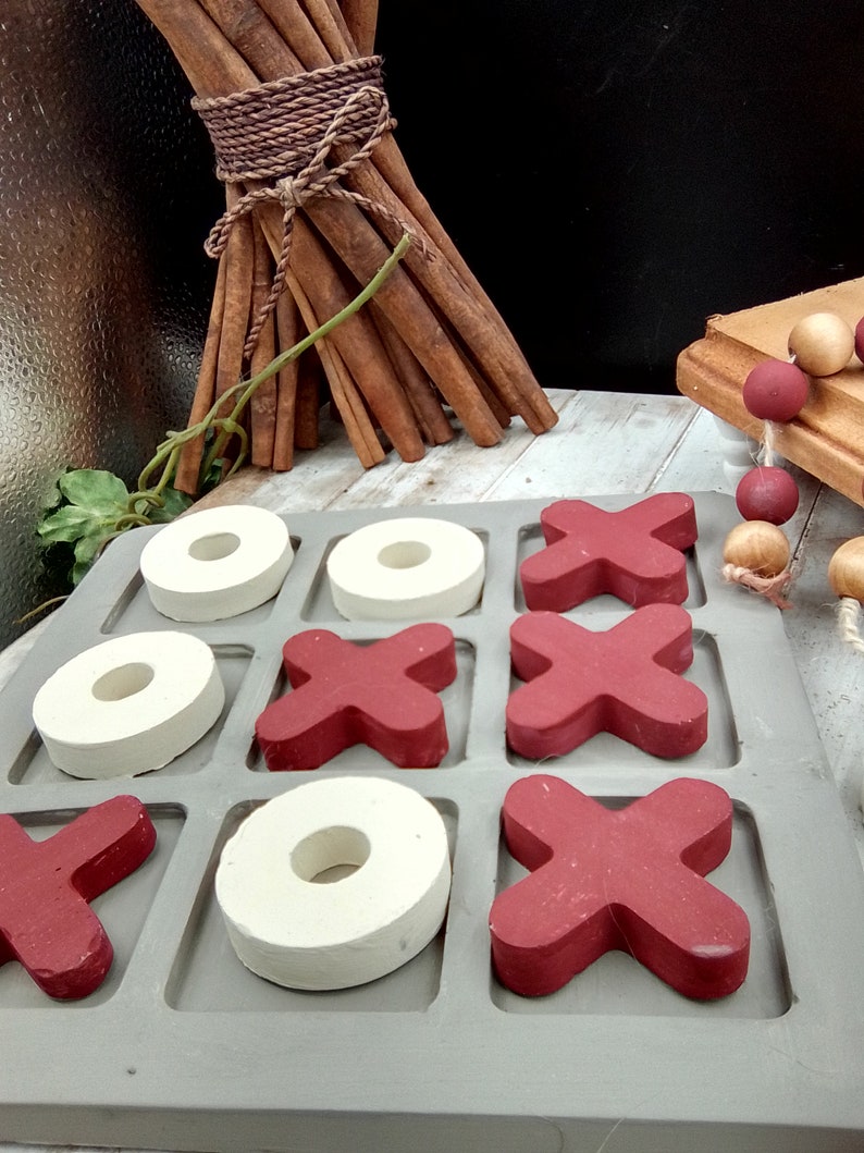 May include: A gray wooden tic-tac-toe game with red X's and white O's. The game is set up on a gray surface.