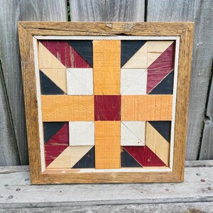 May include: A framed wooden quilt block with a geometric pattern in red, black, white, and orange. The quilt block is made of wood and has a rustic look.