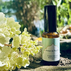 May include: A small, clear glass bottle with a black cap and a white label. The label says "Amor & Psyche" and "Taboikaa Brume de Parfum 30 ml".