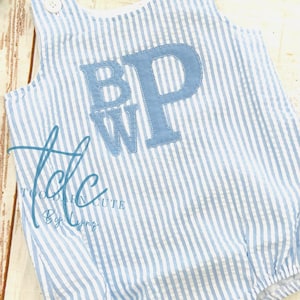 May include: A blue and white striped baby onesie with the letters "BWP" embroidered on the front in blue thread. The onesie has a white collar and snaps at the bottom.