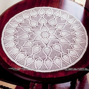 May include: A round, off-white crochet doily featuring an intricate, repeating leaf-like pattern radiating from the center. The delicate, hand-crafted textile displays a complex openwork design with fine thread detailing throughout the circular piece.