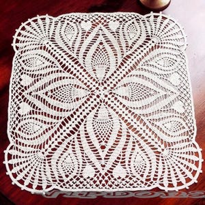 May include: A square white crochet doily featuring an intricate, symmetrical pattern of repeating leaf-like motifs and openwork mesh. The design radiates from a central point, creating a detailed geometric structure with scalloped edges.
