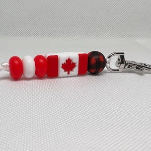 May include: A red, white, and black beaded keychain with a Canadian flag charm and a silver lobster clasp.