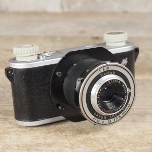 May include: A vintage Kodak camera with a black textured body and silver top plate. The lens assembly features a silver ring with text reading Kodak Anastigmat Special f/3.5 50mm and Dakon Shutter. Two white knobs are on the top.