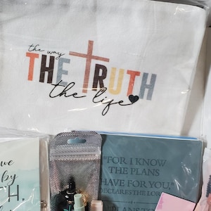 Może przedstawiać: Asortyment przedmiot&oacute;w religijnych, w tym pł&oacute;cienna torba z napisem "THE TRUTH the life", sk&oacute;rzany brelok do kluczy z napisem "Let Your Light Shine" i dziennik z napisem "For I know the plans I have for you".
