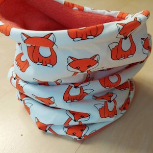 Könnte beinhalten: Ein weißer Halsschmuck mit einem sich wiederholenden Muster aus orangefarbenen Füchsen. Der Halsschmuck ist mit einem einfarbigen orangefarbenen Stoff gefüttert.