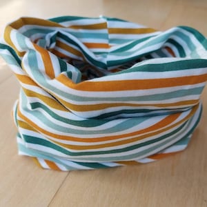Könnte beinhalten: Ein gestreifter Stoff-Halswärmer in den Farben Weiß, Grün und Orange. Der Stoff ist gefaltet und zu einer Röhre gerollt.
