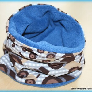 Könnte beinhalten: Ein blauer, mit Fleece gefütterter Halsschmeichler mit einem braunen und weißen gemusterten Stoff, der ein sich wiederholendes Muster aus kleinen Fahrzeugen zeigt.