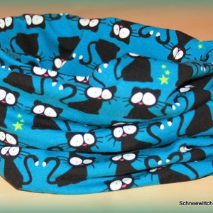 Könnte beinhalten: Ein blauer Stoff-Halswärmer mit einem sich wiederholenden Muster aus schwarzen Katzen. Die Katzen haben weiße Augen und schauen in verschiedene Richtungen.