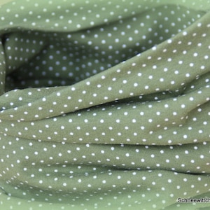 Könnte beinhalten: Ein grüner Stoff-Halswärmer mit weißen Punkten.