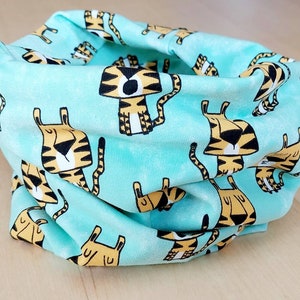 Könnte beinhalten: Ein türkisfarbener Stoff-Halswärmer mit einem sich wiederholenden Muster aus gelben und schwarzen Comic-Tigern.