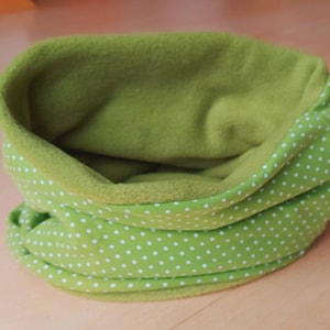 Könnte beinhalten: Ein lindgrüner Fleece-Schlauchschal mit weißem Polka-Dot-Muster auf der Außenseite. Die Innenseite ist einfarbig lindgrün. Der Schlauchschal ist über sich selbst gefaltet.